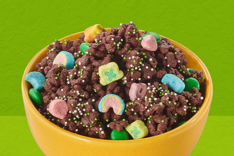 Chocolate Lucky Snack Mix topped with chocolate candies and nonpareils in a yellow bowl.