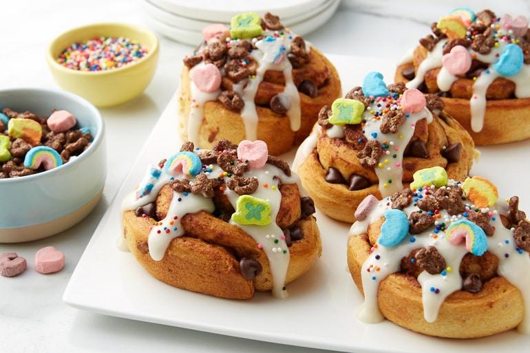 Five Breakfast Rolls topped with Chocolate Lucky Charms™ Cereal served on a white plate.