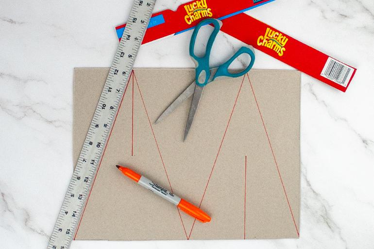 Step 5 of the cereal box Christmas trees with a pen, scissors and ruler resting upon the cardboard.
