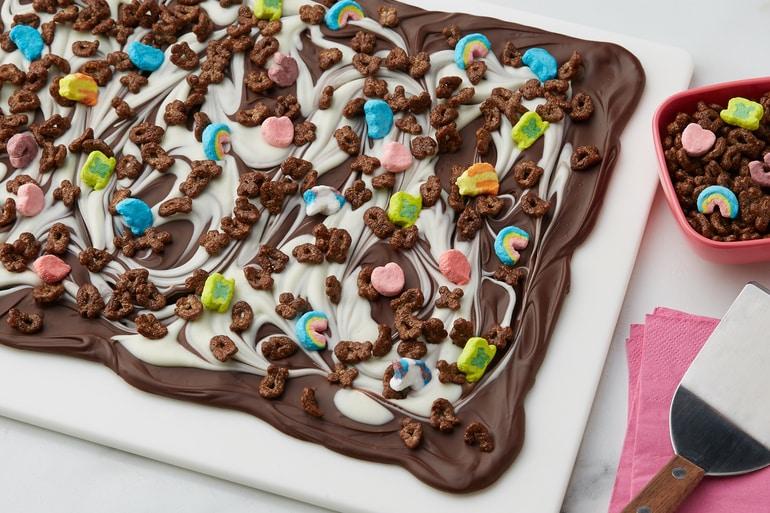 Receta de corteza de chocolate espolvoreada con Lucky Charms™ en una bandeja de hornear blanca.