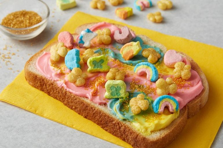 Tostada Lucky Charms Leprechaun en una servilleta amarilla con untable de arcoíris y cereal Lucky Charms™ Honey Clovers.