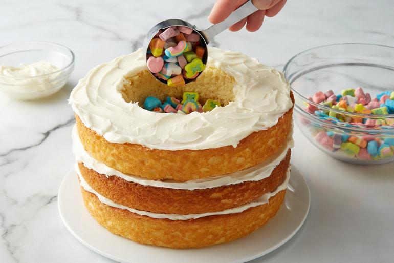 Preparación de Lucky Charms™ Leprechaun Rainbow Layer Cake con cereales Lucky Charms™ Marshmallow Clusters en el centro.