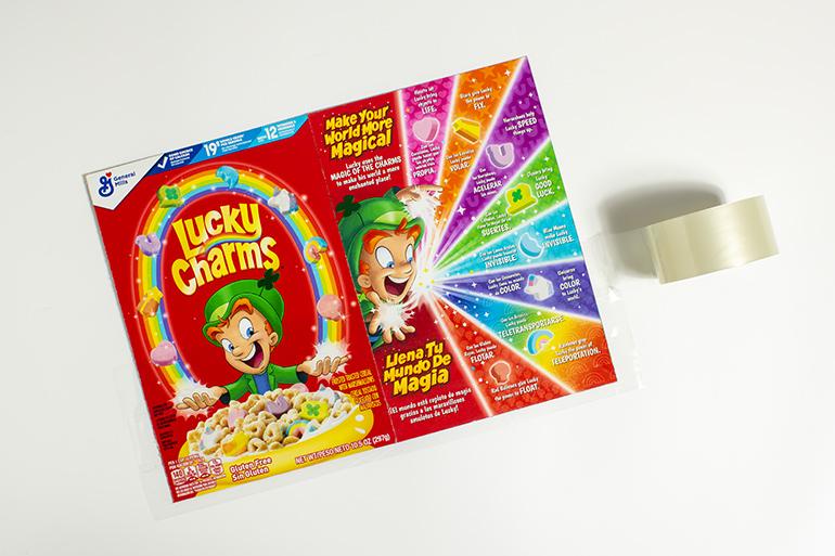 Una bandeja de barras de galletas glaseadas Lucky Charms sobre una tabla de servir blanca, todas cortadas en cuadrados iguales. Hay malvaviscos esparcidos al lado de la tabla.