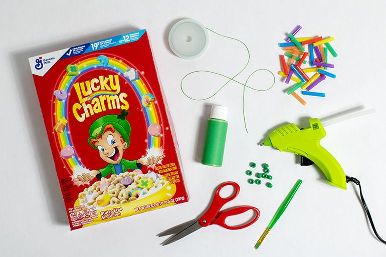 Paso 1 para construir el collar de la buena suerte, mostrando los amuletos recortados de una caja de Lucky Charms con unas tijeras.