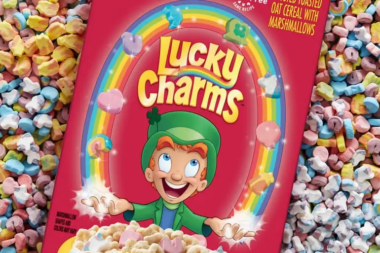 A box of Lucky Charms cereal laying in a pile of Lucky Charms marshmallows