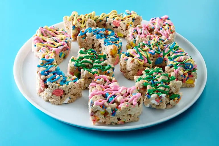 Vibrantly-colored No-Bake Lucky Charms™ Cereal Bar Cutouts on a white plate with blue background.