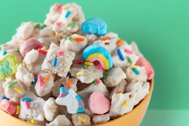 Lucky Charms™ Leprechaun Snack Mix topped with candy sprinkles in a yellow bowl on a green background.