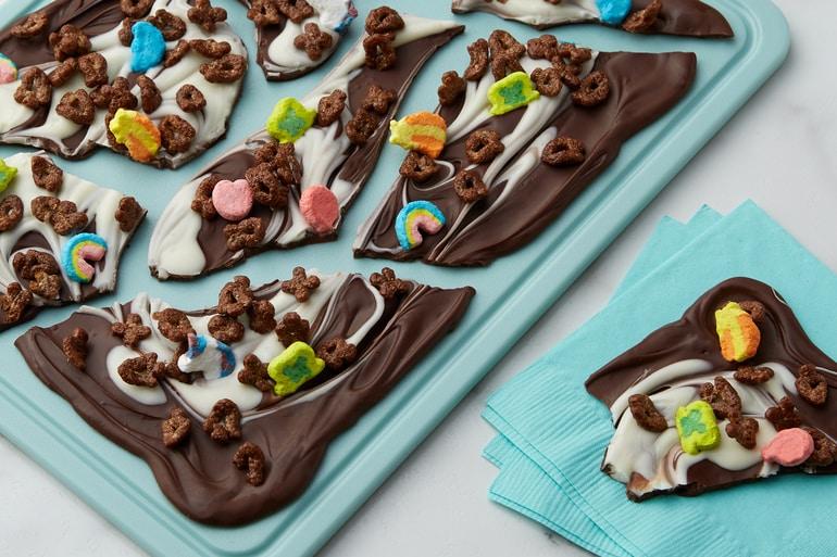Broken up Swirled Chocolate Bark topped with Chocolate Lucky Charms™ served on a cutting board and teal napkins.