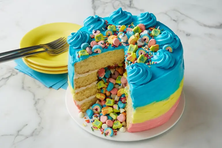 Frosted Lucky Charms™ Leprechaun Rainbow Layer Cake sliced open to expose cereal filling.
