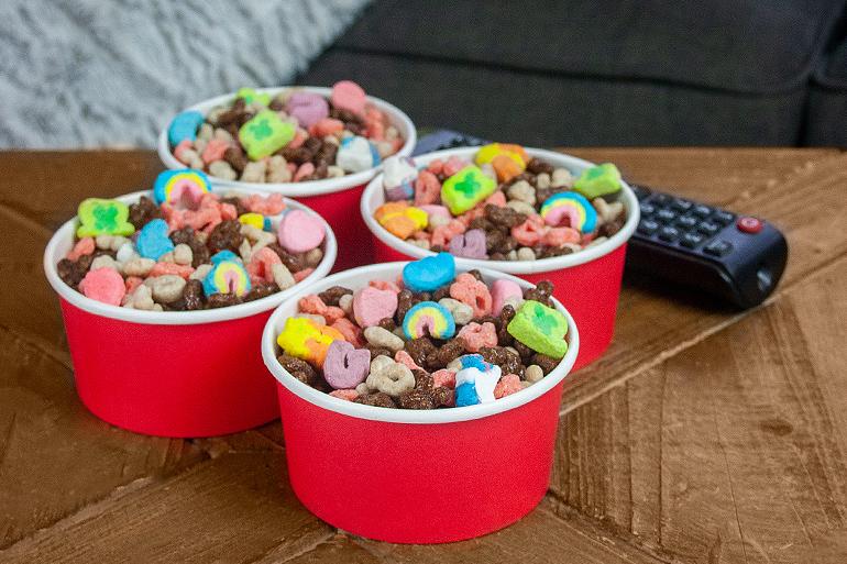 Four tubs of Lucky Charms™ Movie Night Snack Mix recipe next to a remote control.