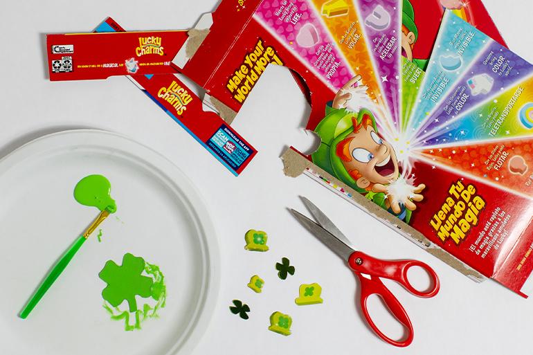 Lucky Charms™ Good Luck Charm Necklace Step 1 showing charms cut out from a box with a scissors.