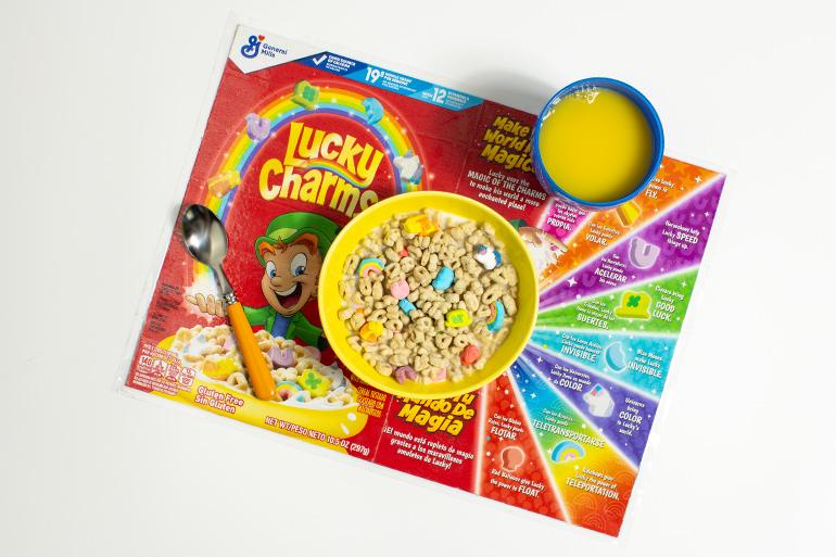 An overhead shot of a placemat made from a Lucky Charms™ cereal box under a bowl of cereal and a glass of orange juice.