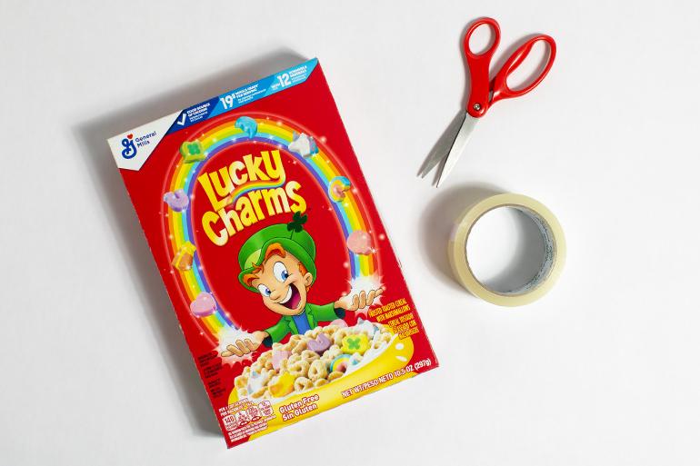 Supplies needed for a placemat, a Lucky Charms™ Cereal box, scissors, and tape.