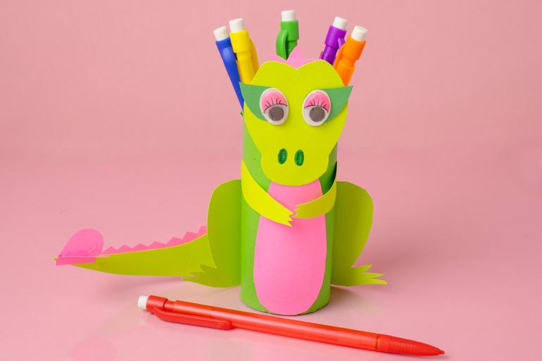 A Lucky Charms™ Dragon Pencil Holder made from brighly colored construction paper in front of a red mechanical pencil.