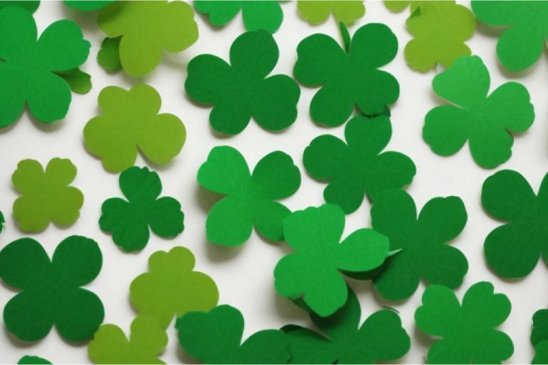 A collection of three and four leaf clovers scattered about with space between each clover so that the white background can still be seen.