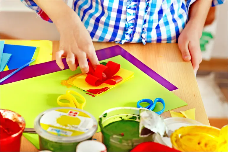 Child engaged in arts and crafts with colorful paper and painting supplies.